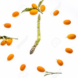 A clock face shaped out of kumquats with green asparagus tips for pointers. All elements are isolated on white, i.e. cut out.