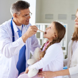 Mature doctor checking up throat of cute girl with her mother near by